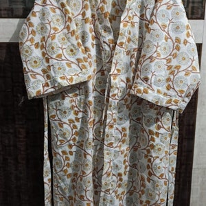 May include: A white cotton robe with a floral print in shades of brown and blue. The robe has a tie belt and three-quarter sleeves.