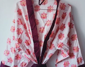 Puede incluir: Una bata de algodón blanca con ribete burdeos y estampado floral. La bata tiene un cinturón de atar y mangas largas.