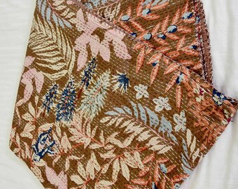 May include: A brown kantha quilt with a floral pattern in shades of pink, blue, and orange. The quilt is folded in half and has a frayed edge.