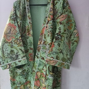 May include: A green floral print robe with white piping. The robe has a long sleeve and a shawl collar.