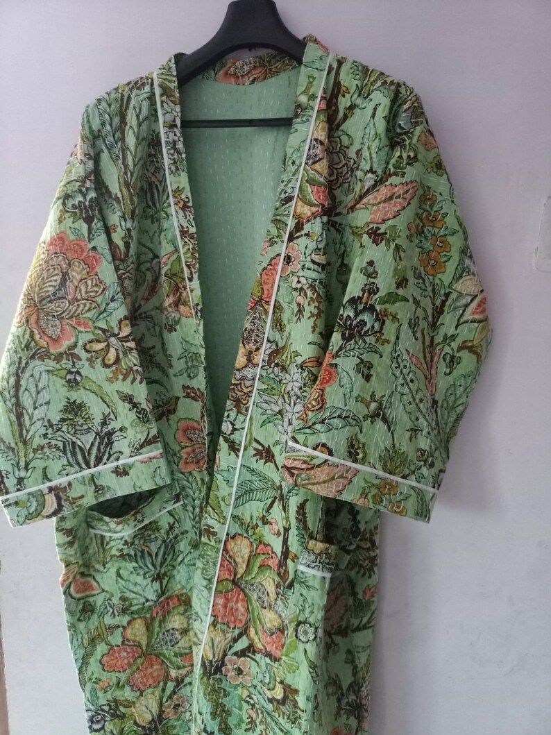 May include: A green floral print robe with white piping. The robe has a long sleeve and a shawl collar.