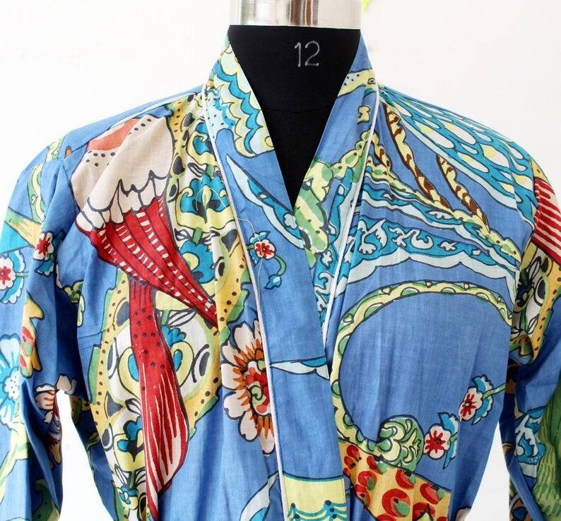 Puede incluir: Una bata de algod&oacute;n azul con ribete blanco y estampado floral y de p&aacute;jaros de colores. La bata tiene un cuello de estilo japon&eacute;s tradicional.