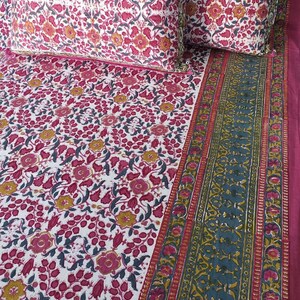Può includere: Un set di biancheria da letto a fantasia floreale con sfondo bianco, fiori rosa e gialli e foglie verdi. Il set comprende un lenzuolo piano, un lenzuolo con angoli e due federe. Il bordo ha un design verde acqua e rosso.