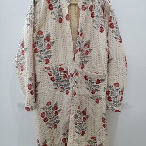 May include: Cream-colored, quilted robe with a floral pattern in red and blue. The robe has a relaxed fit, long sleeves, and two pockets. The floral design is repeated across the robe, and the stitching is visible.