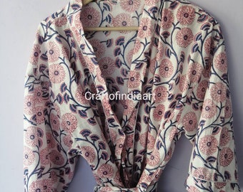 Puede incluir: Una bata de algodón blanca con estampado floral rosa y azul. La bata tiene cuello chal, cinturón de atar y mangas tres cuartos.