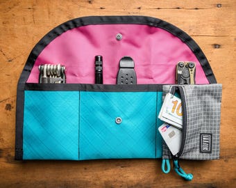 May include: A turquoise and pink zipped pouch with a variety of tools and cash inside. The pouch has a zipped pocket on the outside and a flap that closes with a snap.
