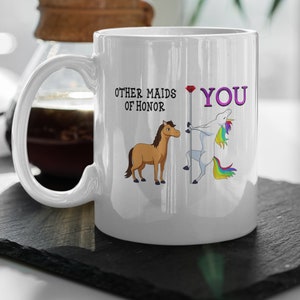 May include: White ceramic mug with a unicorn and a horse illustration. The text on the mug reads "Other maids of honor. You."