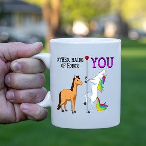 May include: White ceramic mug with a unicorn and a horse illustration. The text on the mug reads "Other maids of honor" and "You" with a pink diamond between the two phrases.