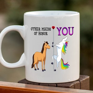 May include: White ceramic mug with a unicorn and a horse illustration. The text on the mug reads "Other maids of honor YOU".