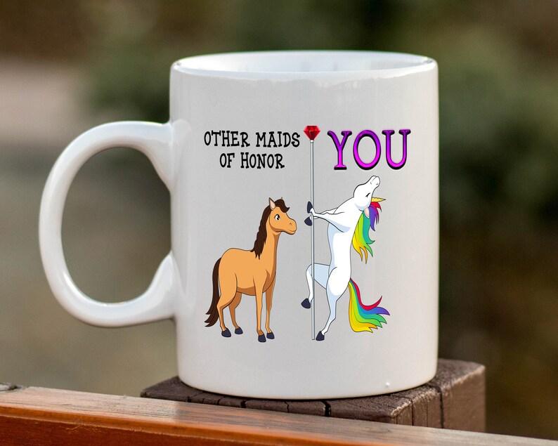 May include: White ceramic mug with a unicorn and a horse illustration. The text on the mug reads "Other maids of honor YOU".