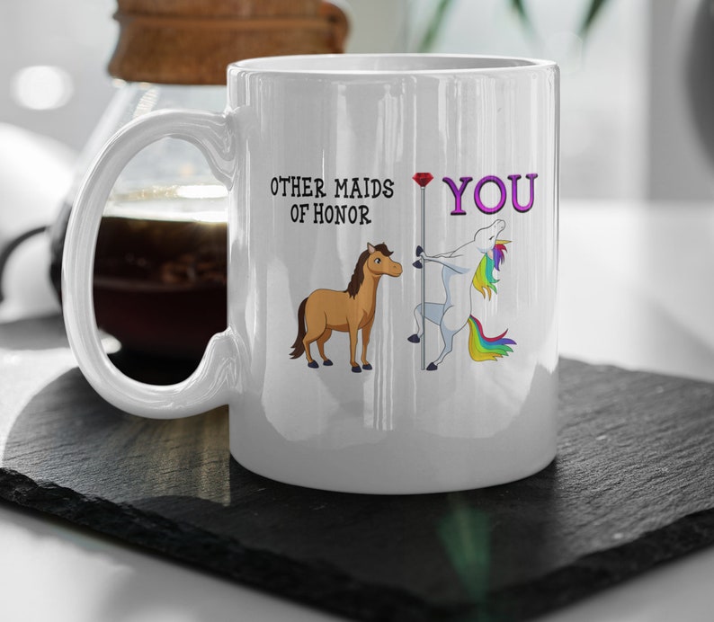 May include: White ceramic mug with a unicorn and a horse illustration. The text on the mug reads "Other maids of honor. You."