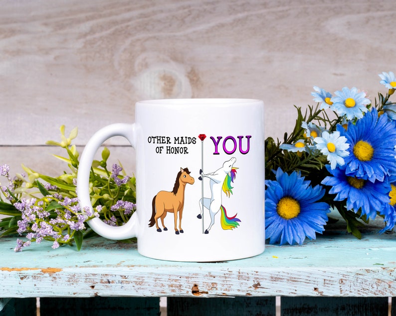 May include: White ceramic mug with a cartoon unicorn and horse. The mug reads "Other maids of honor YOU" with a red heart between the words.
