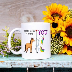 May include: White ceramic mug with a humorous illustration of a horse and a unicorn. The text on the mug reads "Other maids of honor" and "You".