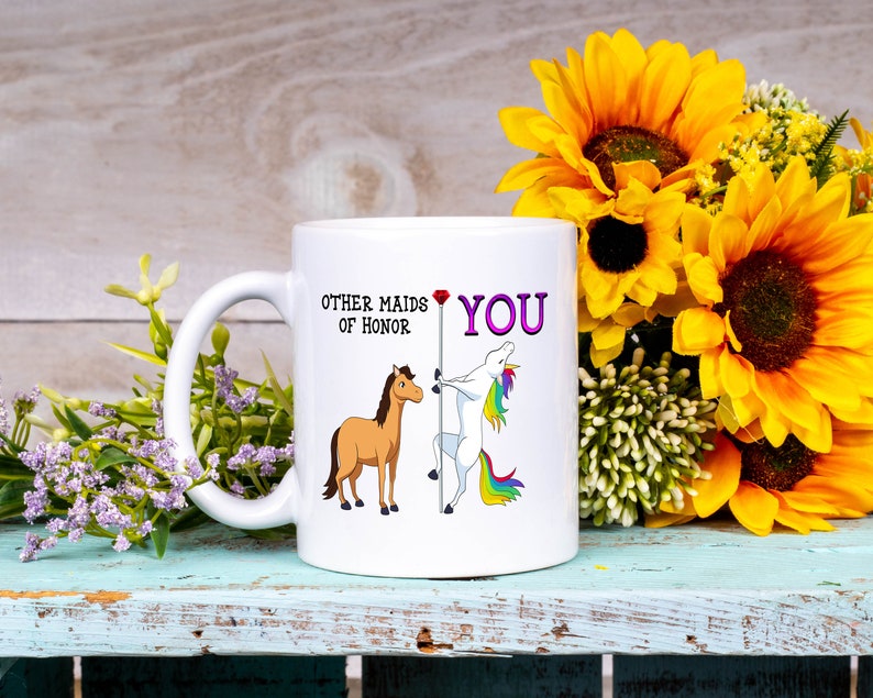 May include: White ceramic mug with a humorous illustration of a horse and a unicorn. The text on the mug reads "Other maids of honor" and "You".