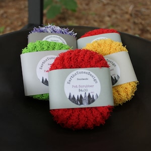 May include: Four handmade pot scrubbers in a black bowl. The scrubbers are made of colorful yarn and are labeled "Earth Tones Design" with the price of $4.00.