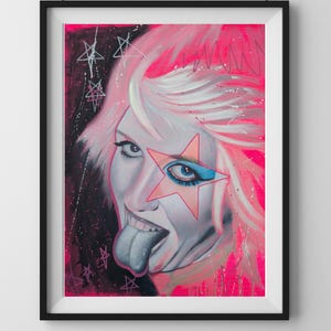 May include: Framed artwork featuring a portrait of a person with white hair and a star-shaped eye patch. The person is sticking out their tongue, and the background is a vibrant pink with star accents. The artwork is in a black frame.