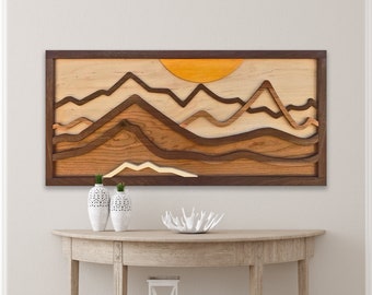 Puede incluir: Una pieza de arte de pared de madera que representa una cordillera en capas con un sol amarillo en el fondo. Las montañas están hechas de diferentes tonos de madera marrón, y el sol está hecho de una madera más clara.