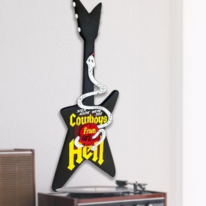 May include: Black electric guitar shaped like a star with a white snake wrapping around it. The guitar has the words "Step Aside Were The Cowboys From Hell" written on it in yellow letters.