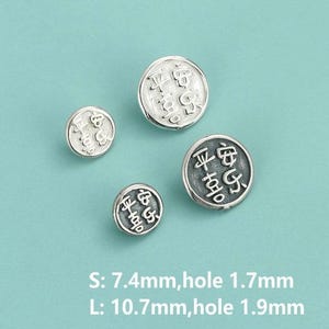 May include: Four small, round, silver charms with embossed Chinese characters. The charms vary in size, with the larger ones measuring 1.07cm in diameter and the smaller ones 0.74cm. The background is a solid, light teal colour.
