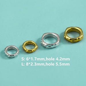 Puede incluir: Cuatro anillos plateados y dorados de diferentes tamaños se muestran sobre un fondo azul claro. Los anillos tienen una superficie texturizada e irregular. El texto de la imagen indica los tamaños: S: 6*1,7 mm, agujero 4,2 mm y L: 8*2,3 mm, agujero 5,5 mm.