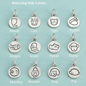 Può includere: Una collezione di ciondoli rotondi color argento, ognuno con un animale diverso dello zodiaco cinese. I ciondoli includono un topo, una mucca, una tigre, un coniglio, un drago, un serpente, un cavallo, una pecora, una scimmia, un gallo, un cane e un maiale. Testo: 8mm, foro per anello 3,2mm.