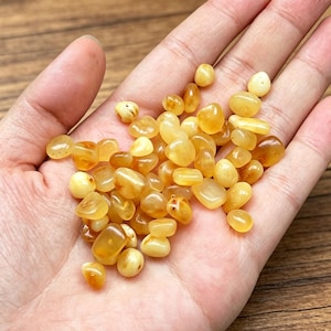 May include: A collection of small, polished amber stones in various shades of yellow, gold, and honey. These smooth, translucent, and opaque pebbles feature irregular, rounded shapes and a glossy finish, showcasing natural variations in colour and texture.