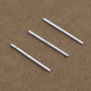 May include: Three silver bar earrings. The earrings are simple and minimalist, with a straight bar design.