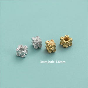 Peut inclure: Quatre perles en forme de fleur, argentées et dorées. Les perles mesurent 3 mm de diamètre avec un trou de 1,8 mm. Le texte sur l'image indique "3mm, trou 1.8mm".