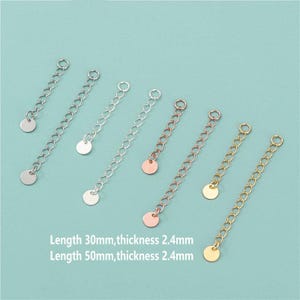 Könnte beinhalten: Eine Sammlung von Schmuckkettenverlängerungen in Silber-, Roségold- und Goldtönen. Jeder Verlängerer hat eine kleine Scheibe und eine Kette mit einem Ring am Ende. Der Text gibt Längen von 30 mm und 50 mm bei einer Dicke von 2,4 mm an.