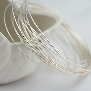 May include: A close-up of a bundle of silver wire, arranged in a circular shape. The wire is thin and delicate, and it is coiled together in a neat and organized fashion.
