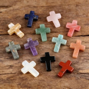 May include: A collection of small, colorful gemstone crosses in various colors, including blue, pink, green, and orange. The crosses are displayed on a rustic wooden surface, showcasing their polished surfaces and unique textures.