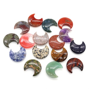 May include: A collection of crescent-shaped gemstones in various colors and patterns. The stones include shades of red, green, purple, and speckled designs. The polished surfaces reflect light, showcasing the natural variations in the materials.