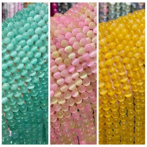 May include: Three strands of gemstone beads are displayed, in teal, pink, and yellow. The round beads have a polished finish. The beads are strung together, creating a colourful display. The image highlights the texture and colour variations of the beads.