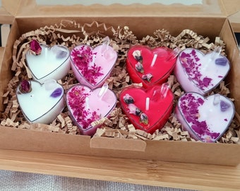May include: A set of eight heart-shaped candles in a brown box. The candles are in shades of pink, red, and white, and each has a small crystal embedded in the center. The candles are surrounded by shredded paper.