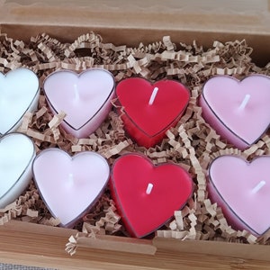 Könnte beinhalten: Eine Schachtel gefüllt mit herzförmigen Teelichtern in Rosa, Weiß und Rot. Die Teelichter sind in einem Gittermuster angeordnet und von zerkleinertem Papier umgeben.