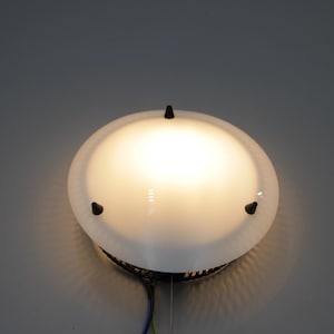 Könnte beinhalten: Eine weiße Deckenleuchte mit einem runden, mattierten Glasschirm und drei schwarzen Metallakzenten.