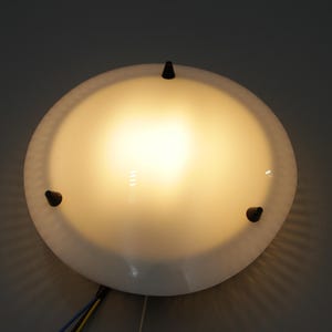 Könnte beinhalten: Eine weiße Deckenleuchte mit einem runden, mattierten Glasschirm und drei schwarzen Metallakzenten.