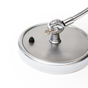 May include: A chrome desk lamp with a round base and a flexible arm. The lamp has a black on/off switch on the base.