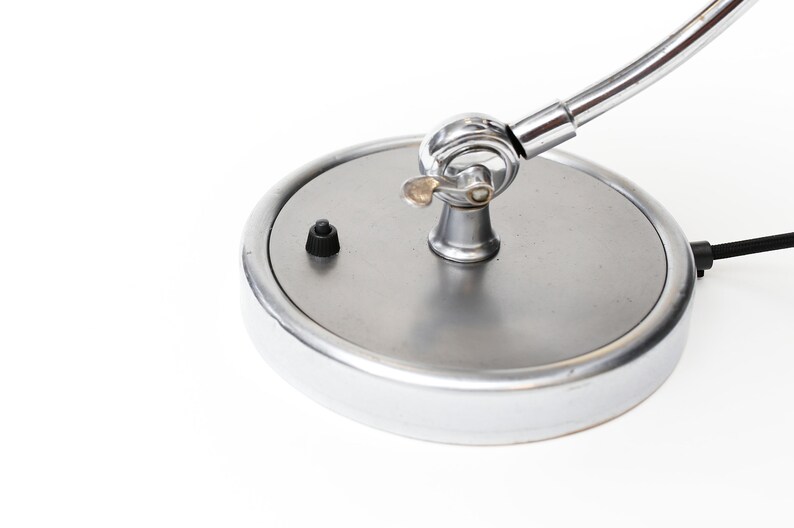 May include: A chrome desk lamp with a round base and a flexible arm. The lamp has a black on/off switch on the base.