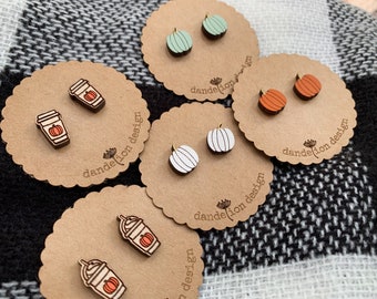 Könnte beinhalten: Vier Paar Holzohrringe auf braunen Karten mit dem Text "dandelion design". Die Ohrringe sind in Form eines Kürbisses, einer Kaffeetasse und eines Kürbisses mit Stiel.