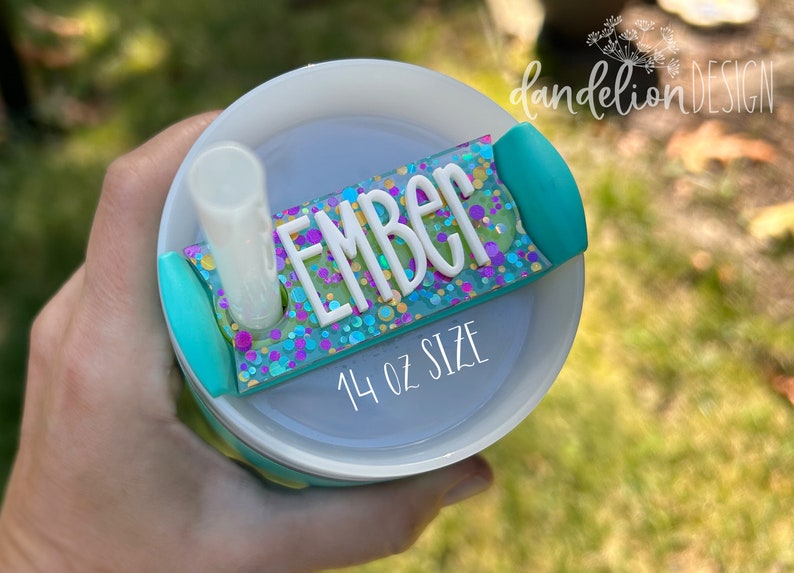 May include: A turquoise and white 14 oz tumbler with a clear straw and a turquoise and glitter name tag that says "EMBER".
