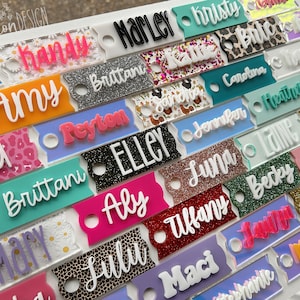 May include: A collection of colorful, personalized name tags with various glitter and patterned backgrounds. The names include Syd, Amy, Marley, Brittani, Peyton, Elley, Aly, Lulu, Tiffany, Maci, Luna, Jennifer, Carolina, Heather, Lane, Becky, Lilly, Jessie, and  more.