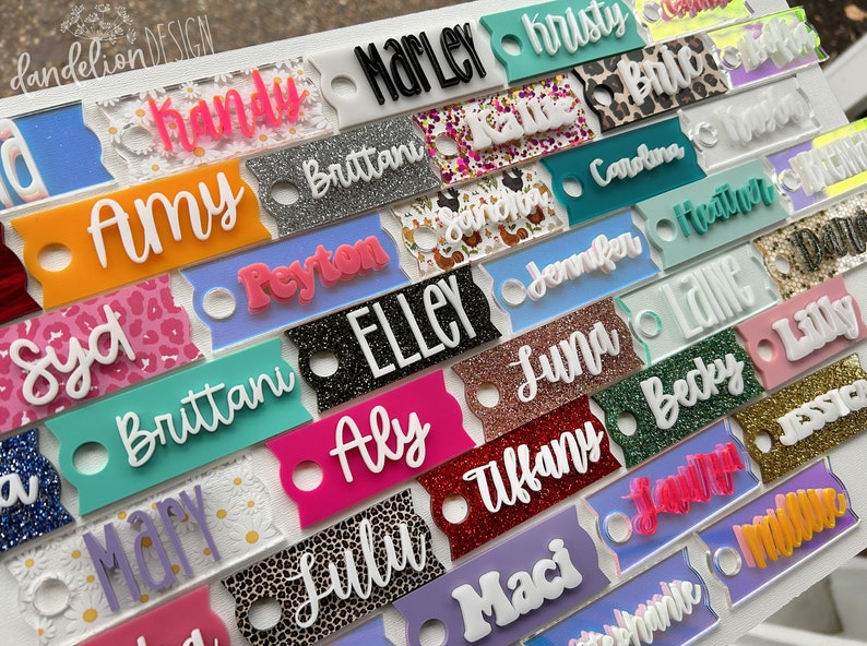 May include: A collection of colorful, personalized name tags with various glitter and patterned backgrounds. The names include Syd, Amy, Marley, Brittani, Peyton, Elley, Aly, Lulu, Tiffany, Maci, Luna, Jennifer, Carolina, Heather, Lane, Becky, Lilly, Jessie, and  more.