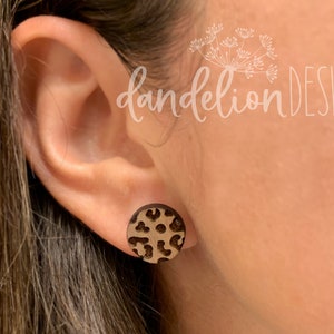 May include: A pair of brown wood stud earrings with a leopard print design.