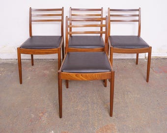 May include: Four mid-century modern dining chairs. The chairs have a dark brown leather seat and a wooden frame. The backs of the chairs have a ladder-back design. The chairs are made of a light brown wood.