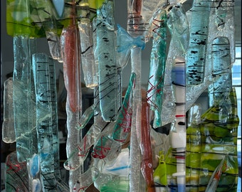 May include: Abstract art piece made of glass with various colors and textures. The glass pieces are layered and overlapping, creating a sense of depth and movement. The colors include green, blue, red, and white.