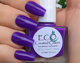 May include: A bottle of purple nail polish with a white cap. The bottle is labeled "ECO Created Colors handmade nail polish 10 Free Cruelty Free Vegan 10.5ml/.35 oz e".