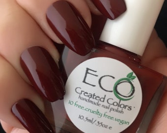 May include: A bottle of dark red nail polish with a white label that reads "Eco Created Colors: handmade nail polish 10 free.cruelty free.vegan 10.5ml/.35oz e"