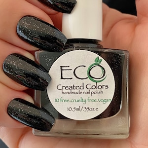May include: Black nail polish with a sparkly finish in a clear glass bottle with a white cap. The bottle label reads "ECO Created Colors handmade nail polish 10 free. cruelty free. vegan. 10.5ml / .35oz e".