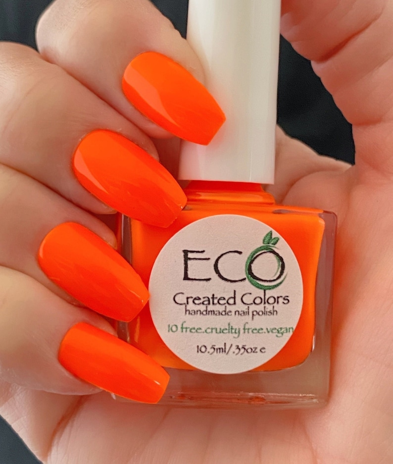 May include: A bottle of bright orange nail polish with a white label that says "ECO Created Colors handmade nail polish 10 free. cruelty free. vegan. 10.5ml / .35oz"
